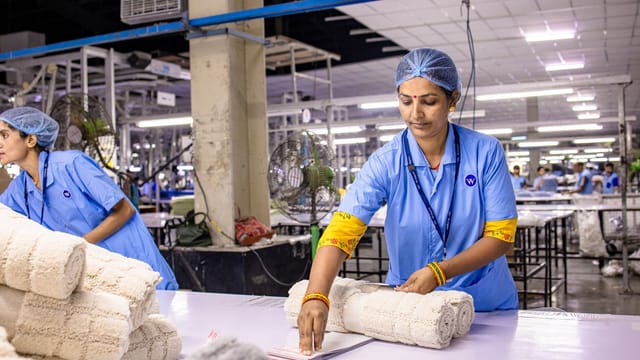 Indian textile worker organizing fabric rolls in a factory setting.