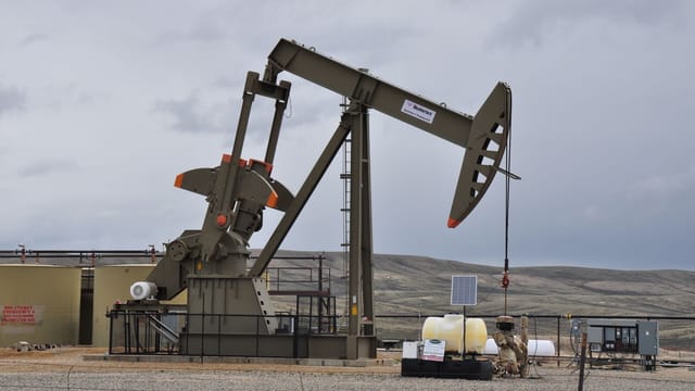 Oil pump jack and equipment at remote industrial site under cloudy sky.