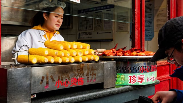 A vibrant street food scene with grilled corn and skewered meats in Beijing's markets.