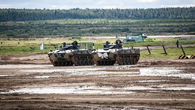 Two military tanks on a muddy field during a cloudy day, showcasing combat readiness.