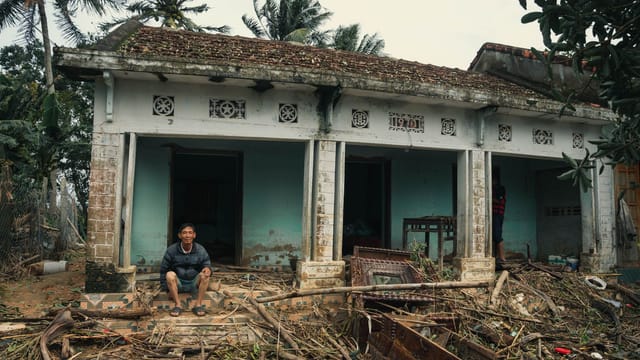 A man sits outside his flood-damaged home surrounded by debris in Phú Yên, Vietnam.