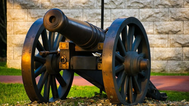 Antique cannon on display against a stone wall backdrop during fall.