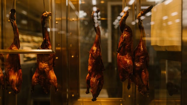 Hanging roasted ducks in a warm-lit display case, showcasing Asian street food tradition.