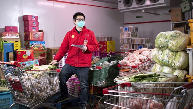 Asian man wearing red jacket and mask working in a store with shopping carts in Wuhan, China.