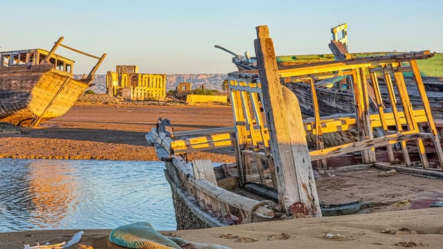 Rustic wooden ships resting on Bushehr's shoreline under the warm sunset light.