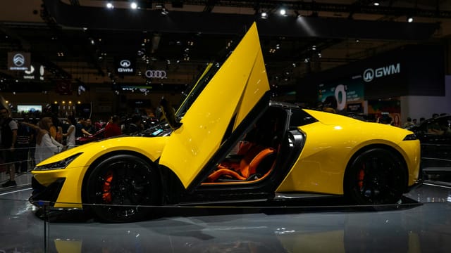 A sleek yellow sports car with butterfly doors showcased at an auto exhibition.