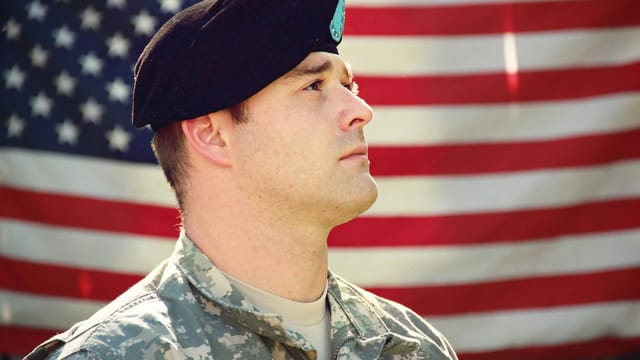 US soldier in uniform stands proudly with the American flag in the background, capturing a sense of patriotism.