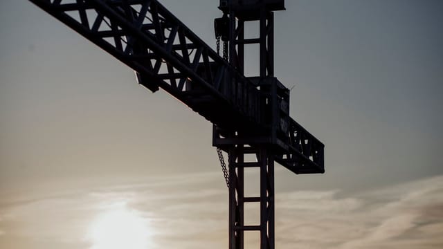 Dramatic silhouette of a construction crane against a sunset sky, capturing industrial beauty.