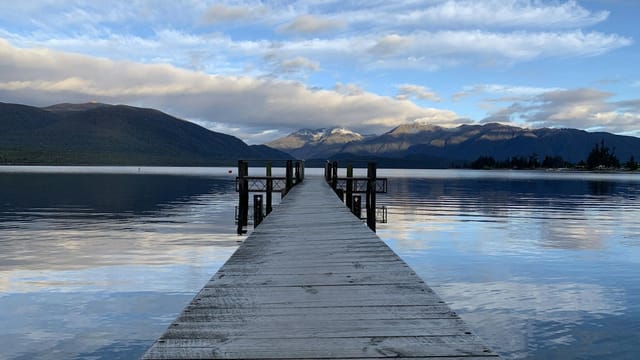 Tranquil boardwalk leading to a serene lake in Southland, with mountainous backdrop.