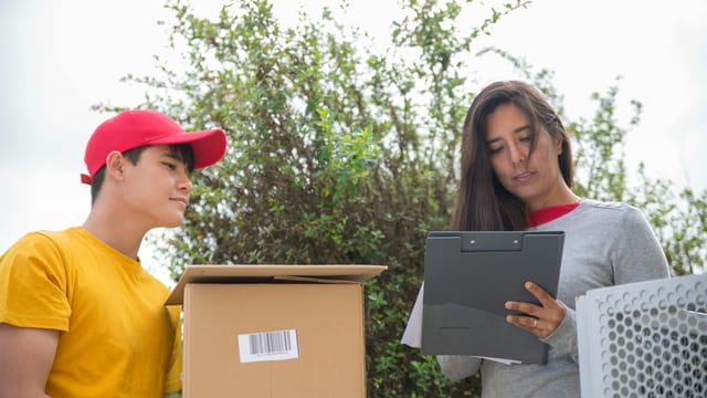 Courier delivering a package while a woman signs a form outdoors.