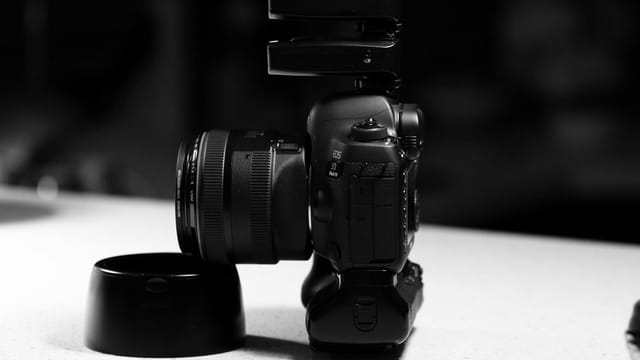 Monochrome side view of a DSLR camera with flash on a white tabletop, ideal for photography concepts.