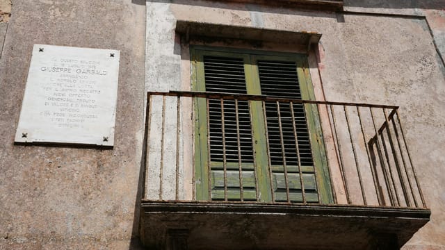 Rustic Italian balcony in Erice, Sicily featuring a Giuseppe Garibaldi plaque.