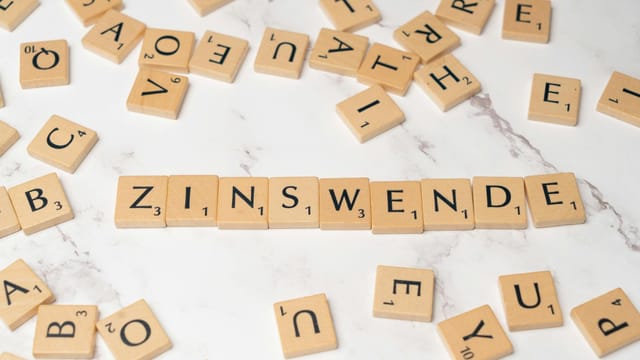 Scrabble tiles arranged to spell 'Zinswende' on a marble surface with scattered tiles around.