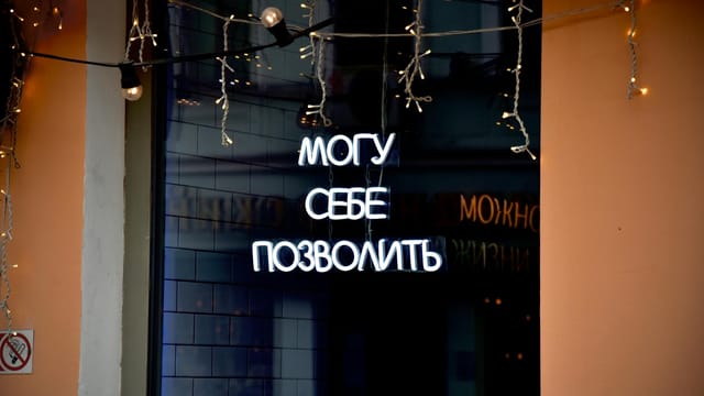 Neon sign in Russian with decorative string lights at night.