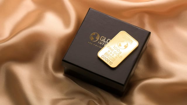 A pristine gold bar resting on a luxurious black box atop a smooth silk fabric.
