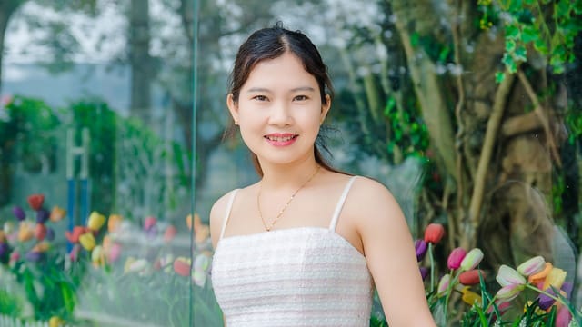 Young woman smiling with colorful flowers in outdoor setting, conveying happiness.