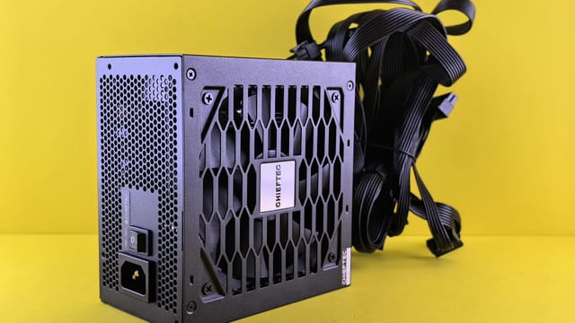 Black Chieftec power supply unit with cables against a vibrant yellow background.