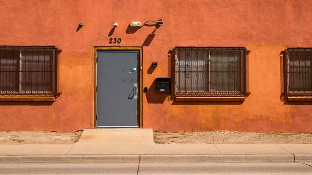 An orange facade with a sturdy metal door and barred windows under bright daylight.