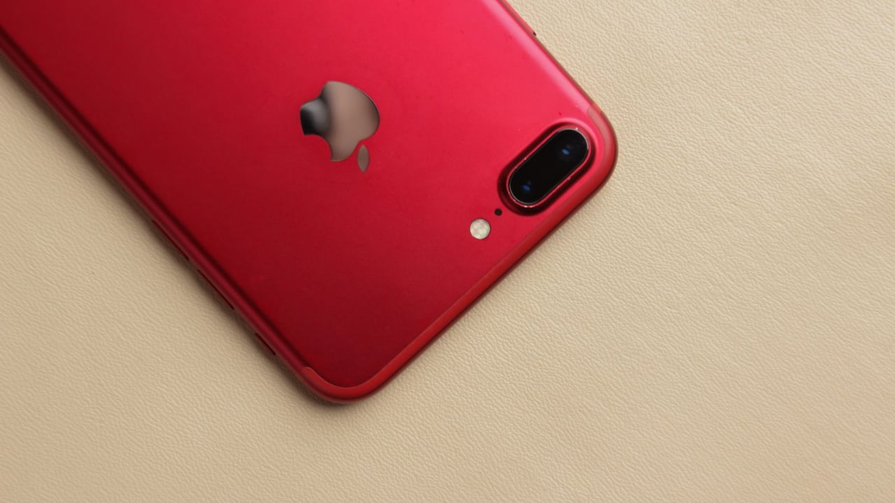 A vibrant red smartphone with a reflective logo on a neutral beige background, highlighting its modern design.