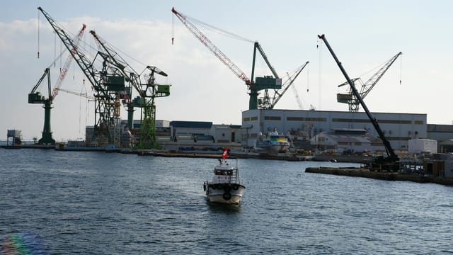 View of Kobe port featuring large cranes and a boat navigating the waters, ideal for industrial themes.