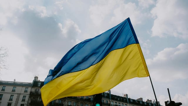 Waving Ukrainian flag against a cloudy sky and city skyline, symbolizing national pride.