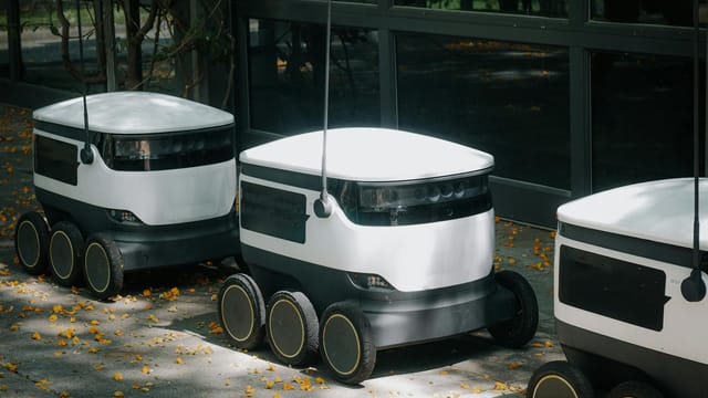 Autonomous delivery robots on a sidewalk during daytime, showcasing modern technology.