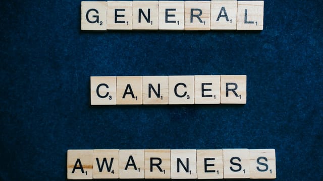 Words 'General Cancer Awareness' spelled with Scrabble tiles on a blue surface, promoting awareness.
