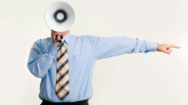 Businessman in blue shirt using a megaphone while pointing, isolated on white background.