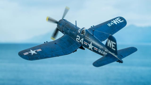 A detailed view of a Corsair fighter plane flying over the ocean, evoking WWII history.
