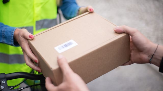 Close-up of hands exchanging a cardboard box outdoors, symbolizing delivery service in Portugal.