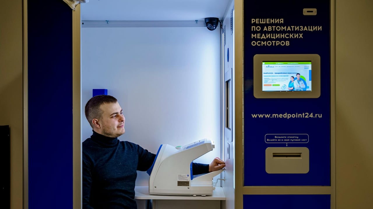 Caucasian man smiling while using automated healthcare booth for blood pressure and health checks.