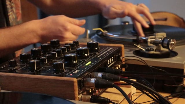 Close-up of a DJ using a turntable and audio mixer for music mixing.