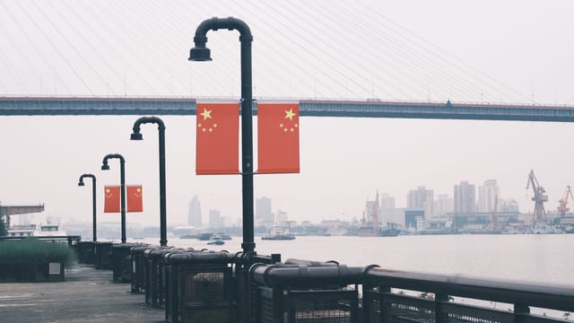 Peaceful view of urban riverfront featuring Chinese flags and a large suspension bridge. Perfect travel scene.