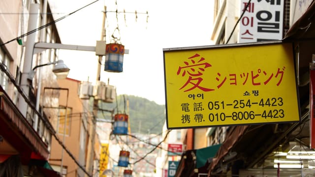 Colorful signboards and bustling street create a lively urban market atmosphere.