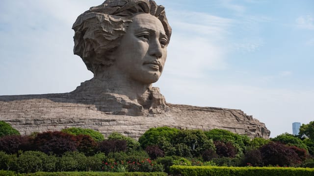 Large stone statue of a prominent figure set amidst a lush park landscape.