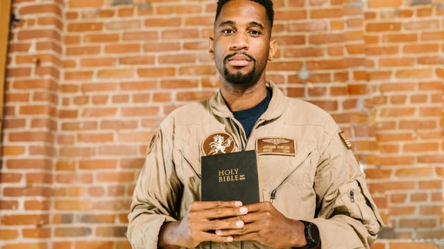 A military veteran holding the Holy Bible in front of a brick wall background.