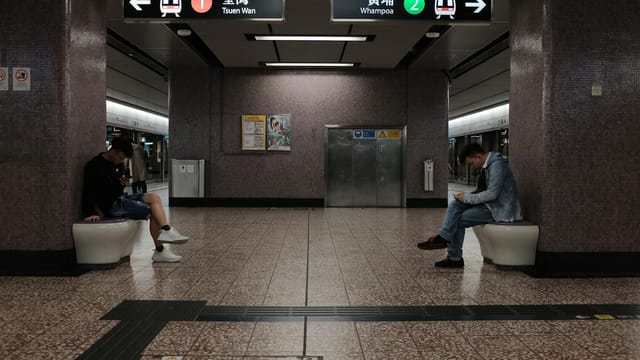 Two men sitting quietly in a Hong Kong subway station, absorbed in their mobile phones.