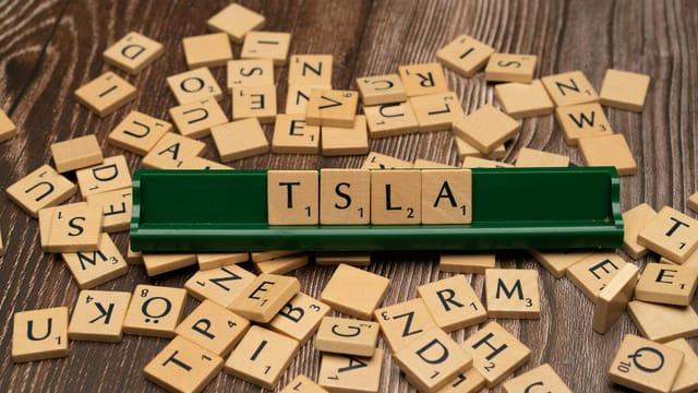 Wooden letter tiles spell TSLA, hinting at the stock market and investment themes.