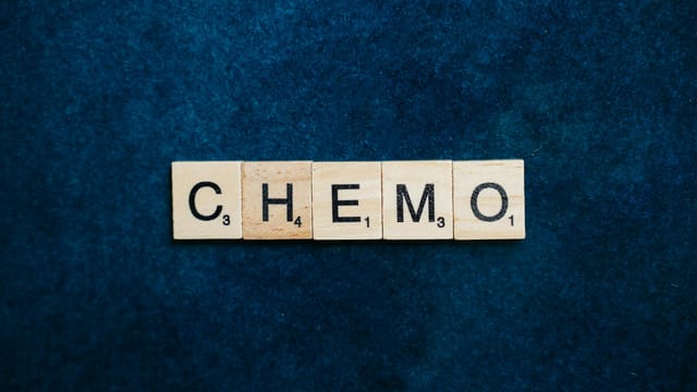 Close-up of Scrabble tiles spelling 'CHEMO' on a dark blue textured background.