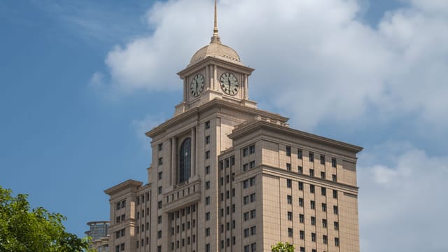 Elegant clock tower atop a government building, framed by clear blue sky and clouds.