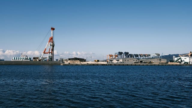 View of an industrial port in Gamagōri, Japan, showcasing cranes and the coastal area under a clear sky.