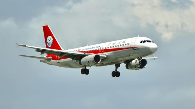 A Sichuan Airlines aircraft gracefully flies through a cloudy sky, showcasing its red and white design.