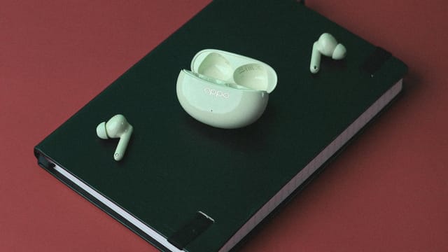 Green notebook and wireless earbuds on red surface, perfect for technology-themed still life.