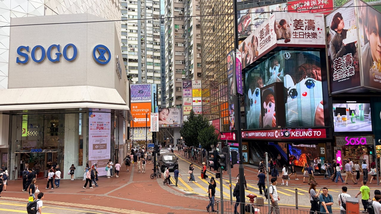 Vibrant city scene depicting a busy street near Sogo Department Store in Hong Kong, with digital billboards and pedestrians.