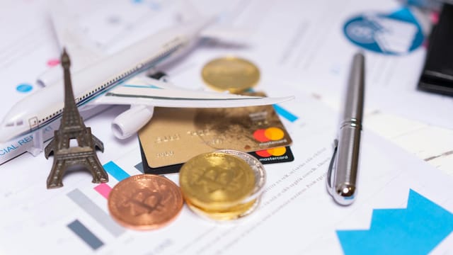 A travel finance concept featuring cryptocurrency, credit card, airplane model, and Eiffel Tower on financial documents.