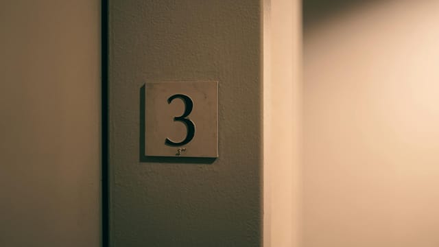 Minimalist photo of a number three sign on a textured beige wall indoors.