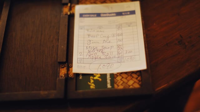 Close-up of a restaurant bill placed on a dark wooden table, creating a moody ambiance.