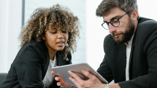 Two business professionals reviewing data on a tablet, fostering collaboration and teamwork in a modern office setting.
