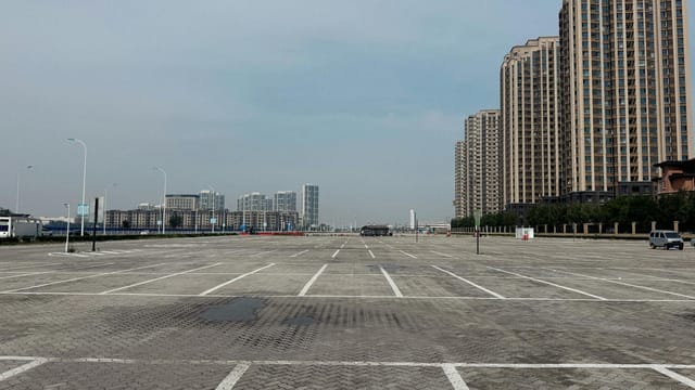 Empty parking lot surrounded by tall residential buildings in an urban setting under a clear sky.