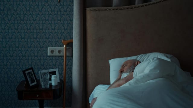 Senior man sleeping in a stylish bedroom with a nightstand and framed photos.